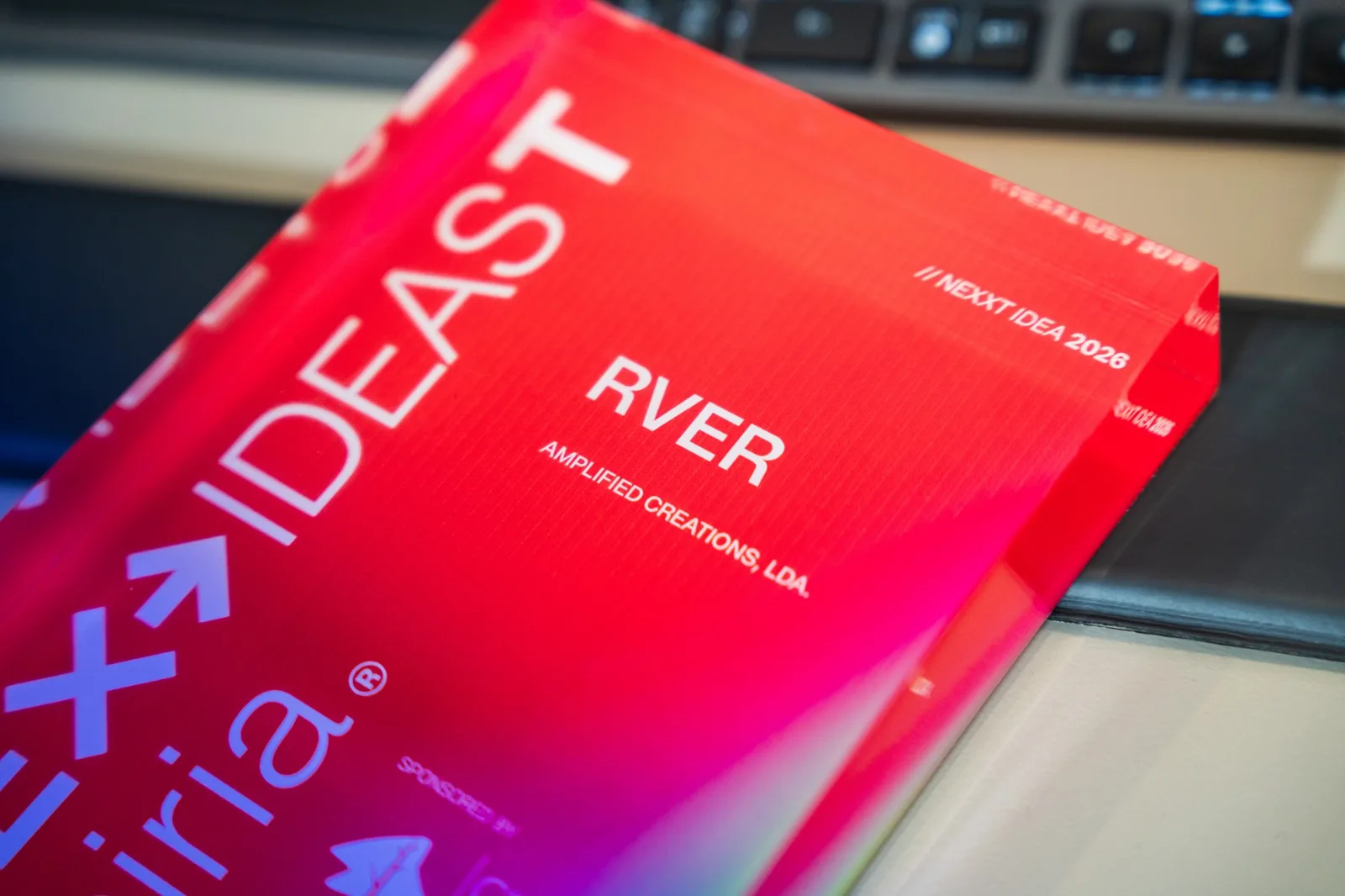 Peça acrílica vermelha do NEXXT Ideas Leiria com a inscrição «NEXXT IDEA 2026 — RVER — Amplified Creations, Lda.».